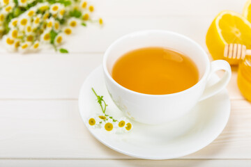 Chamomile tea on a white table. Delicious tonic, soothing and relaxing chamomile tea with chamomile flowers, honey and lemon. Herbal tea for immunity. Close-up.Place for text.Copy space.