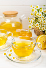 Chamomile tea on a white table. Delicious tonic, soothing and relaxing chamomile tea with chamomile flowers, honey and lemon. Herbal tea for immunity. Close-up.Place for text.Copy space.