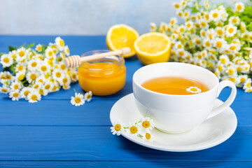 Chamomile tea on a blue table. Delicious tonic, soothing and relaxing chamomile tea with chamomile flowers, honey and lemon. Herbal tea for immunity. Close-up.Place for text.Copy space.