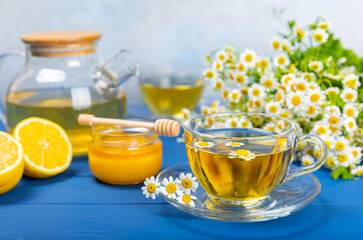 Chamomile tea on a blue table. Delicious tonic, soothing and relaxing chamomile tea with chamomile flowers, honey and lemon. Herbal tea for immunity. Close-up.Place for text.Copy space.