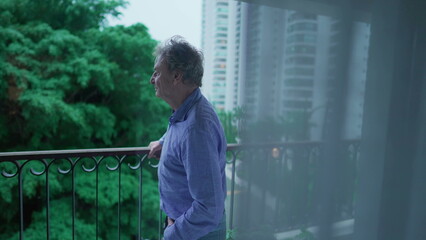 Contemplative Senior Man Lost in Thought, Staring Out from Balcony durign rainy afternoon. Lonely...
