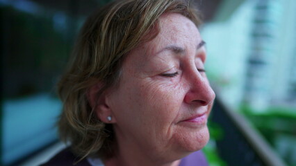 One senior woman closing eyes in contemplation. A meditative older lady opening eyes to sky smiling. person close-up face