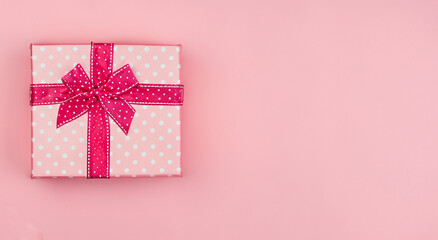 pink gift box with white dots with pink ribbon on pastel pink background in high resolution