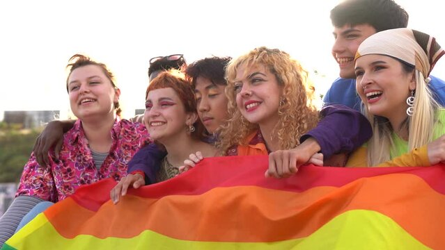 Group of young diverse people holding LGBT rainbow flag outdoor - Multiracial friends having fun together at pride parade
