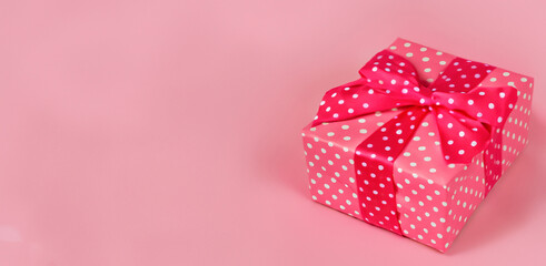 beautiful pink gift box with red ribbon on pink background