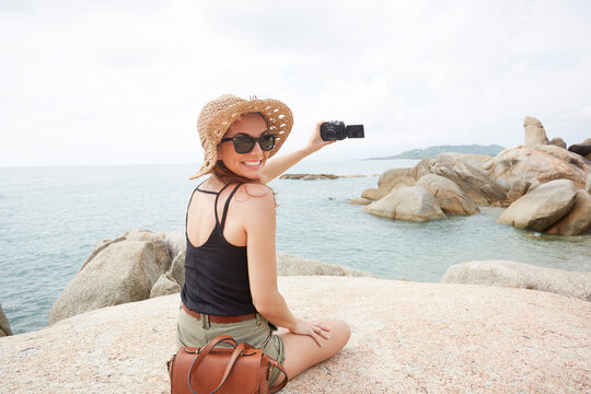 Young woman wearing sunglasses holding camera on rock