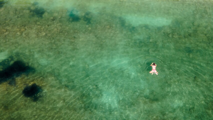 Aerial top view of woman in sea pool water from above, tropical vacation holiday concept. Mediterranean sea. Aerial seascape with woman, clear blue water, waves in summer. Transparent water. 