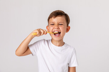 Morning concept. Close-up portrait of a happy laughing little boy with toothbrush on white background. A child in a white T-shirt brushes his teeth on his own. Space for text