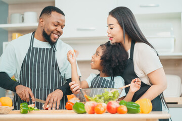 Kind African american parents teaching their adorable daughter how to cook healthy food, free space...