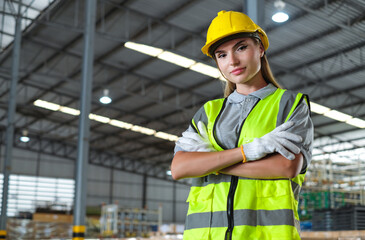 Female industrial engineer in hard hat and safety vest standing confident with arms crossed, productive work in industrial factory.