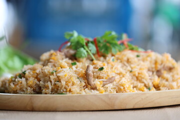 Home made pork fried rice with egg and sliced ​​spring oniontopped with coriander leaves and sliced ​​red chili. Close up the delicious fried rice served on a wooden plate.
