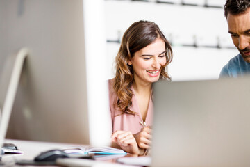 Smiling young businesswoman listening to colleague at desk in office