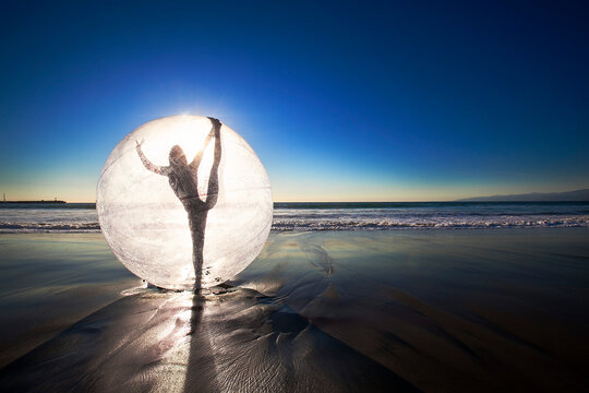 Woman doing yoga in ball on beach during sunset