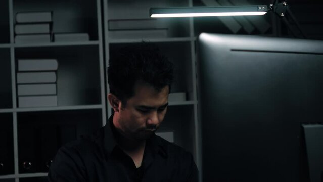 Tired young Asian businessman working overtime in the office room at night, trying to get things done before the deadline.