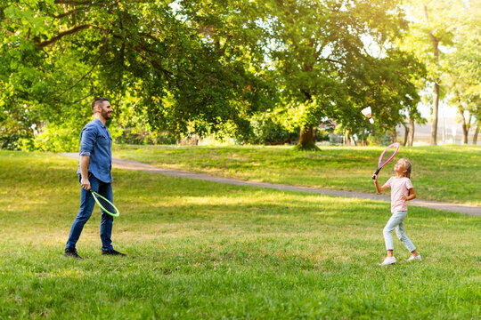 Family pastime. Side view of dad playing badminton with his daughter, holding rackets and using big shuttlecock