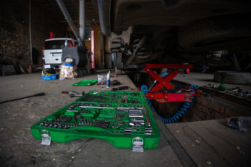 The garage is a small business auto repair shop. Multi-functional auto mechanic's tool set. A car in need of rear axle suspension repair was raised on a hydraulic lift.
