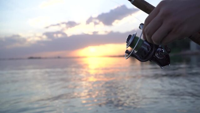 a fisherman spins a fishing rod reel in the sea against the backdrop of sunset