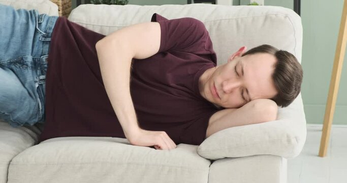 In this tired and drowsy scene, a man is captured dozing off on the sofa in the living room. His face reflects weariness and fatigue, as he seeks some rest and respite from the day's activities.