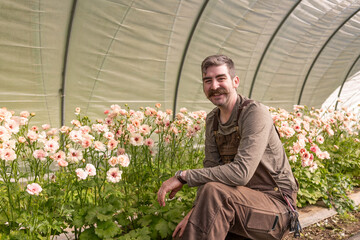 Amid vibrant blooms, a dedicated flower farmer tends to his blossoms in a greenhouse oasis, nurturing nature's beauty.
