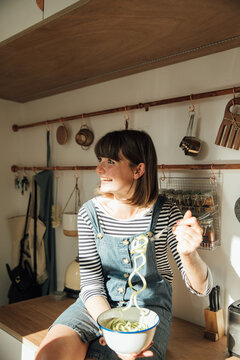 Woman with bowl of zucchini noodles on kitchen bench