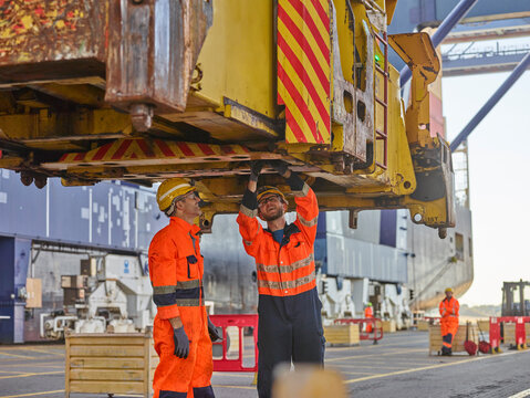 Dock workers repairing crane and loader at port