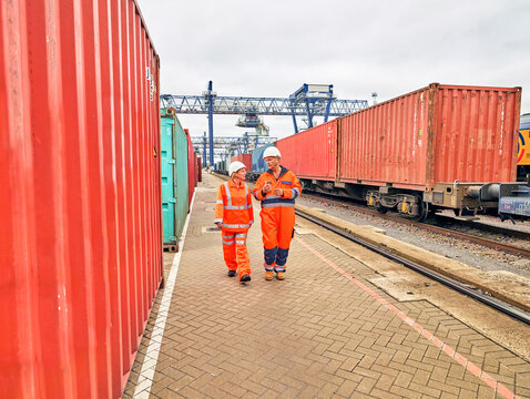 dock workers and manager walking past freight cargo train at port