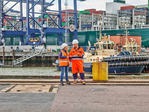 Dock workers standing infront of tug and cargo container ship on digital tablet