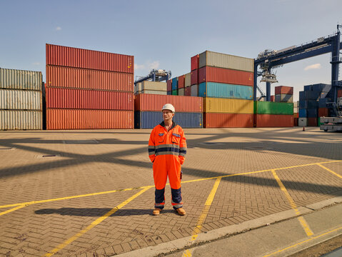 Dock worker in reflective overalls by cargo containers