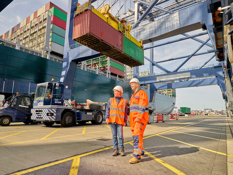 Dock workers by crane lowering cargo container onto truck