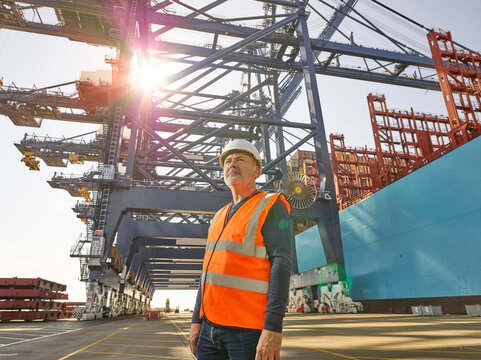 Portrait of dock worker in protective workwear with cargo cranes in background, Felixstowe, England.