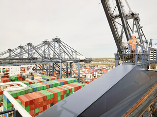 Elevated view of dock worker on cargo crane platform with shipping containers below, Felixstowe, England