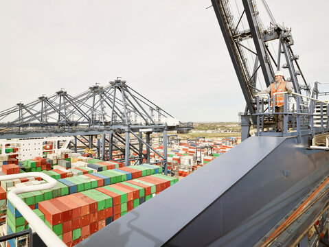 Elevated view of dock worker on cargo crane platform with shipping containers below, Felixstowe, England