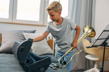 A young boy is putting away his trombone in a case after practicing.