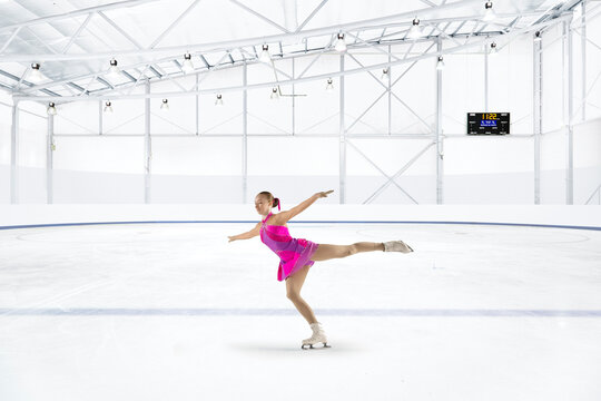Young woman in pink dress figure skating at ice rink
