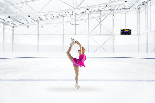 Young woman in pink dress figure skating at ice rink