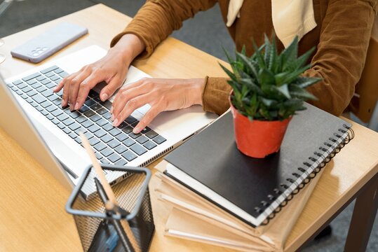 Overview of hands of young businesswoman or student typing on laptop keyboard by desk while working over presentation. View from above