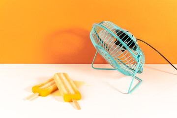 Mango orange ice lollies cooling with a blue little fan on white and orange background