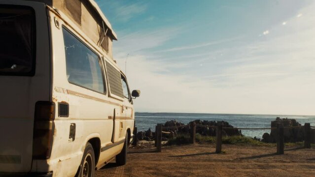 Low angle view of camper van parked on the beach with picturesque scenery view. Concept of nomadic or transient lifestyle, adventure and exploration where people seek freedom and exploration through