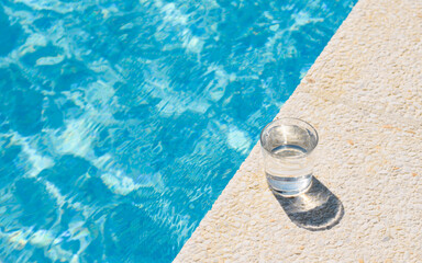 a glass of clean drinking water near the pool on a hot day. Summer vacation concept