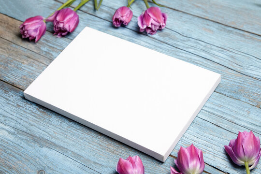 Blank white canvas mockup with flowers on blue background. Picture frame mockup on wooden wall