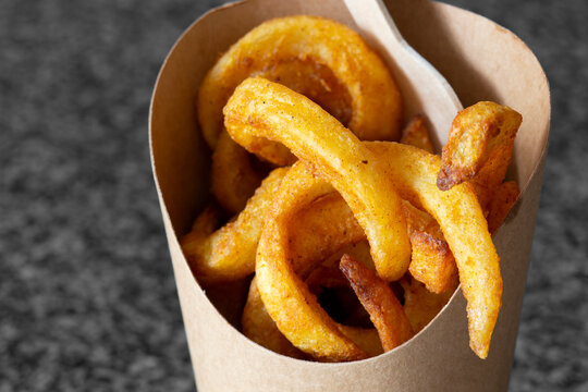 Curly fries takeaway in a cardboard carton with a wooden fork. Biodegradable plastic free eco friendly takeaway container