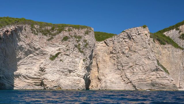 Rock geology layers visible at cliffs near Chomi or Paradise beach at Liapades, Greece, calm green sea in foreground. View from a boat