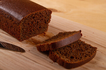 Loaf and sliced portions of dark bread positioned against  light beige wooden background
