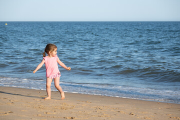 Fototapeta na wymiar toddler baby girl with a pink t-shirt running and playing on the shore of the beach