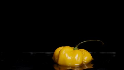A yellow Habanero pepper falls into water with water splashes on a black background, in slow motion. - Powered by Adobe