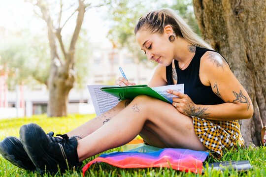 LGTBI College Girl. Modern tattooed girl sitting on top of pride flag at university campus.