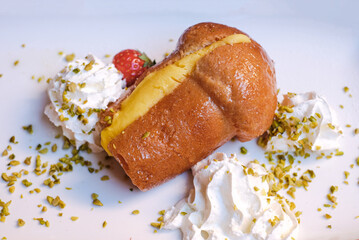 A rum baba filled with pastry cream served with whipped cream, pistachio ground and fresh...