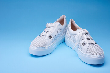 Stylish white sneakers with perforation, thick rubber sole on the gradient blue background. Fashionable sport casual shoes