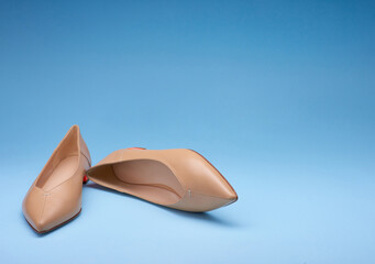 Fancy pointed-toe pastel women's flats on a gradient blue background. One of the shoes is lying on its side. Copy space. Fashion photography