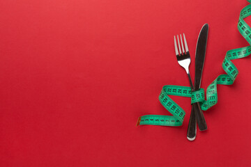 Knife and fork wrapped in tape measure on color background, top view